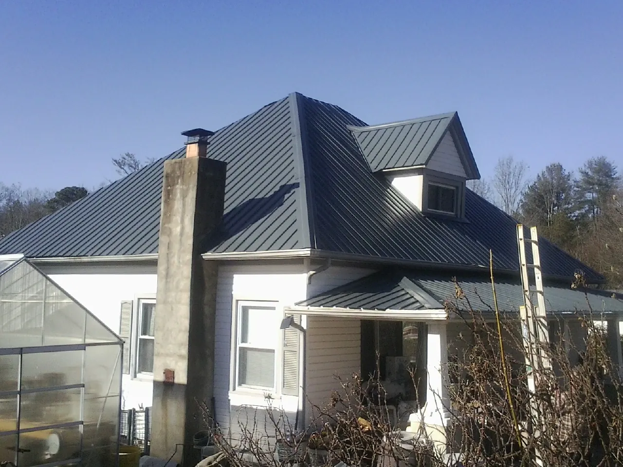 Dark blue standing seam metal roof on a white farmhouse with dormer — Slate & Tile Roof Repair by Roofing Brothers in Angier