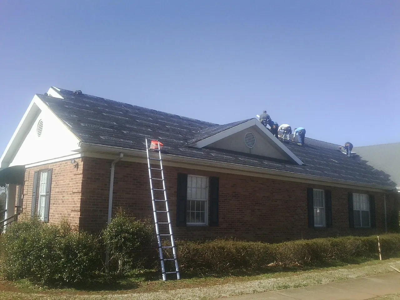 Crew tearing shingles off a brick ranch roof with a ladder set — Emergency Roof Repair work by our crew in Angier