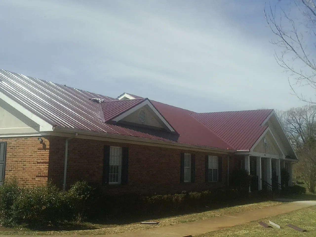 Red metal roof with gabled entries on a long brick building, from a Hail Damage Roof Repair job in Angier