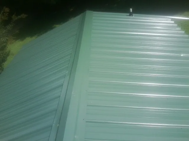 New green metal panels meeting at the ridge of a roof — Flat Roof Repair work by our crew in Angier