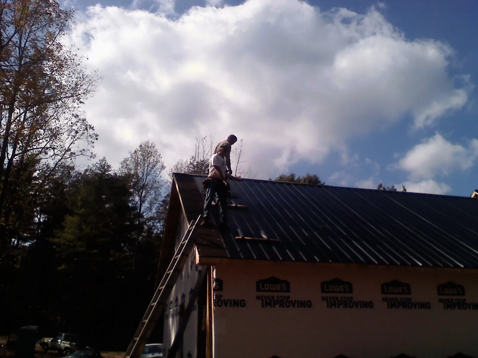Roofer fastening dark metal panels high against a cloudy sky, from a Roof Inspection job in Angier