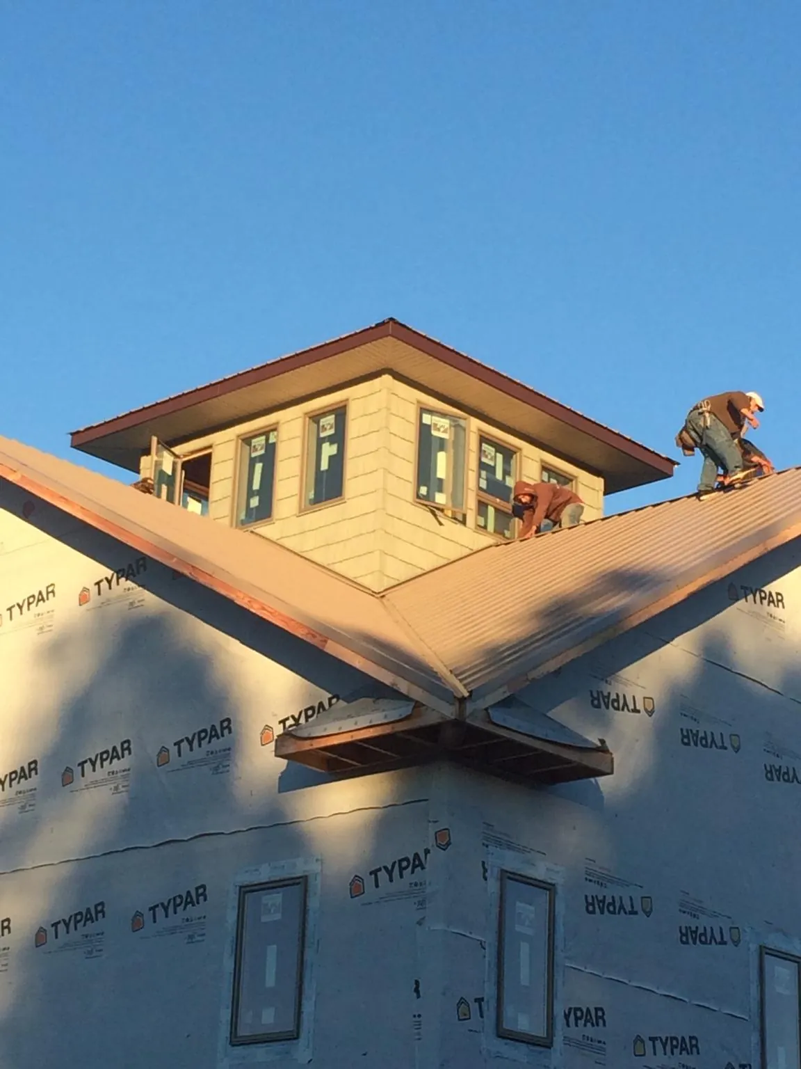 Roofers working around a rooftop cupola on a new metal roof at sunset — Roof Waterproofing in Angier by Roofing Brothers